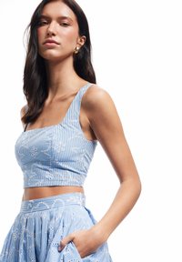 Blauw cropped top met witte bloemenborduursels en verticale strepen. Vierkante halslijn en brede schouderbanden. Gecombineerd met een bijpassende rok.