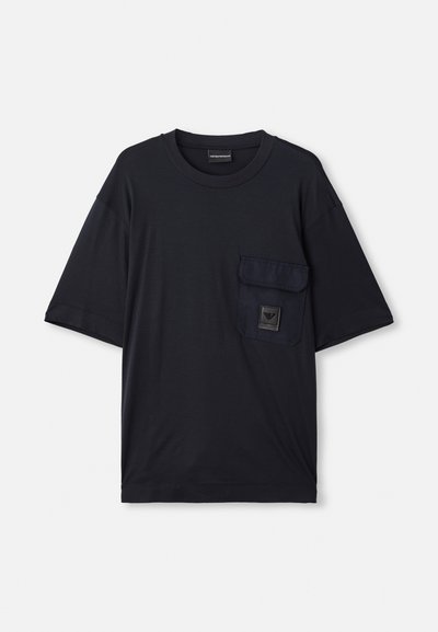Tricou negru cu mânecă scurtă, de tip crew neck, cu un buzunar cu clapă pe partea stângă a pieptului, având o mică etichetă rectangulară cu logo.