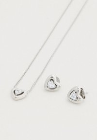 Σετ ασημένιας καρδιάς κοσμημάτων που περιλαμβάνει ένα κολιέ με μενταγιόν και ταίριαστα σκουλαρίκια καρφάκια, το καθένα διακοσμημένο με ένα κεντρικό διαυγές πολύτιμο λίθο.