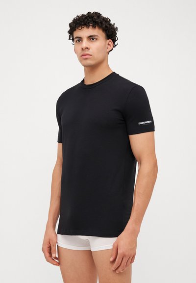 Schwarzes Baumwoll-T-Shirt mit Rundhalsausschnitt und kurzen Ärmeln. Mit einem weißen Logo auf dem linken Ärmel. Glatte Textur, taillierte Passform.