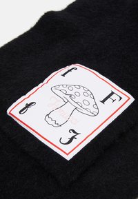 Tessuto nero lavorato a maglia con una trama pelosa, con un'etichetta bianca che mostra un grafico di un fungo e la scritta "Hiorucci" in rosa.