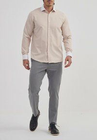 Chemise longue beige clair à rayures verticales, col blanc, associée à un pantalon gris et des chaussures à lacets foncées.