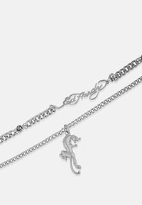 Ασημένια αλυσίδα κολιέ με δύο συνδεδεμένες αλυσίδες, η μία με το λογότυπο "Ed Hardy" και μια κρεμαστή φιγούρα ενός άλματος ζώου.