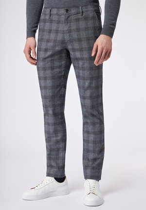 Grijze geruite broek van textuurstof, met een slim fit, riemlussen en een contrasterende knoopsluiting. Gepaarde met witte sneakers.