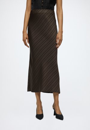 Woman wearing a dark brown satin midi skirt with diagonal stripes and black pointed-toe high heels, standing against a plain background.