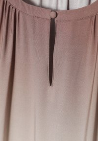Blouse rose pâle avec un col rond, des détails plissés et une petite découpes sous la fermeture du col, avec un bouton recouvert de tissu.