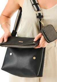 Borsa a mano in pelle nera con finitura testurizzata, dotata di un flap in tessuto intrecciato, accessori in metallo dorato e una pochette zip rimovibile abbinata.