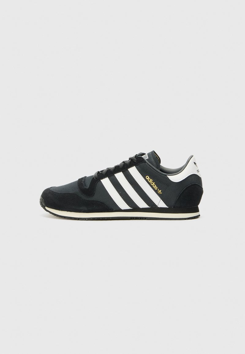 Baskets de sport noires avec des rayures blanches, tige en daim et en mesh, bout rond, laçage sur le devant et accents dorés sur le côté et le talon.