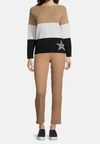 Sweter dzianinowy w poziome paski w odcieniach beżu, bieli i czerni, z detalem w kształcie gwiazdki. W zestawie z beżowymi dopasowanymi spodniami i czarnymi butami wsuwanymi.