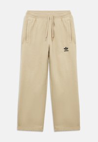 Μπεζ φόρμα με υφή, διαθέτει ελαστική μέση, κορδόνι, πλαϊνές τσέπες και μαύρο λογότυπο Adidas στον αριστερό μηρό.