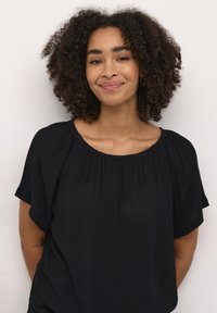 Sort kortærmet bluse med rund halsudskæring, blød tekstur og let indsamling ved skuldrene. Enkelt design uden mønstre eller detaljer.