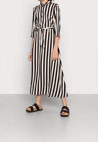 Czarna i kremowa, prążkowana sukienka midi z zapięciem na guziki z przodu, kołnierzykiem, rękawami ¾ oraz wiązanym detalem w talii. Czarne klapki.