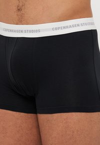 Boxers noirs en tissu doux, avec une taille élastique blanche portant l'inscription "Copenhagen Studios" en gris.