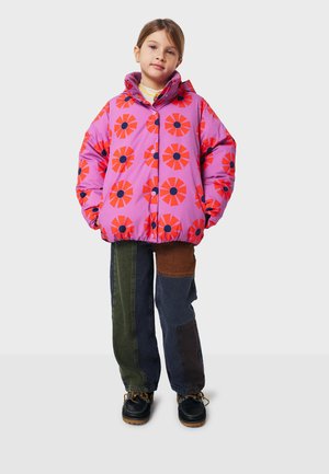Veste en duvet rose vif avec un motif floral rouge et des centres bleu marine, associée à un pantalon en patchwork multicolore et des chaussures noires.