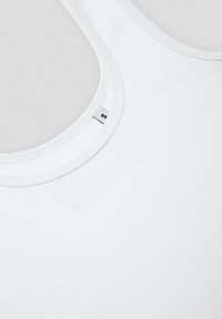 Biała koszulka na ramiączkach z okrągłym dekoltem, wykonana z gładkiego materiału, z małą metką widoczną w pobliżu dekoltu, bez wyraźnych wzorów.