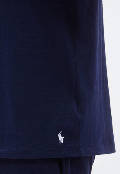 Camiseta de algodão azul-marinho com decote redondo; apresenta um pequeno logótipo branco bordado junto à bainha. Textura macia, design casual.