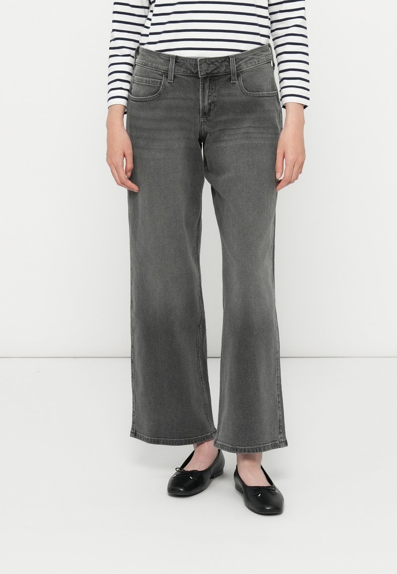 Los vaqueros de pierna ancha en denim gris presentan una cintura alta, cinco bolsillos y un acabado limpio. Combinados con un zapato plano negro y una camiseta a rayas.