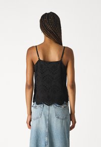 Top sans manches noir avec des détails en broderie œillet, ourlet festonné et bretelles ajustables, associé à une jupe en denim léger.