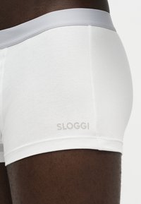 Close-up of a person wearing white Sloggi boxer briefs with a light gray waistband.