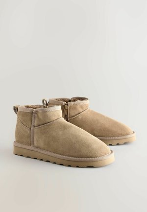 Tanfarbene Wildleder-Stiefeletten mit weichem, plüschigem Innenfutter, Reißverschluss und strukturierter Gummisohle. Rundliche Zehenform und flache Absatzgestaltung.