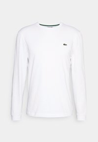 Vit långärmad t-shirt i bomull med rund hals och en liten grön krokodil-logotyp på vänster bröst. Enkelt och figursytt stil.