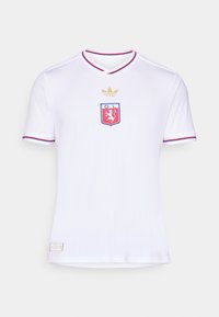 Jersey blanco de manga corta con escote en V, que presenta rayas horizontales, acentos en rojo y azul, un logo bordado y detalles en dorado.