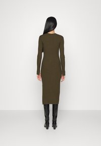 Olivgrön ribbad stickad klänning med långa ärmar och längd till mitten av vaderna, i kombination med svarta klackstövlar. Enkel, kroppsnära design.