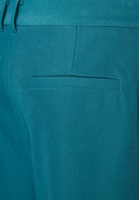 Teal fabric with a smooth, slightly textured finish. Features a single back pocket with a flat design and clean stitching.