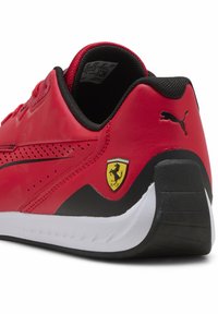 Zapatilla deportiva roja con parte superior de cuero liso, detalles en negro, perforaciones y logo de Puma. Presenta un escudo amarillo de Ferrari en el talón.