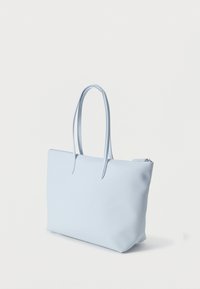 Jasnoniebieska torba na ramię z długimi uchwytami i zamkiem błyskawicznym, przedstawiona na jednolitym białym tle.