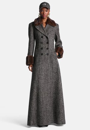 Femme portant un long manteau gris en chevrons avec des boutons croisés, un col et des poignets en fourrure marron, et une casquette noire avec les initiales LS.