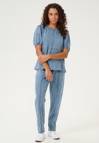 Costum din denim compus din două piese, cu un top cu mânecă scurtă, cu mâneci bufante și talie peplum, asortat cu pantaloni drepți și adidași albi.