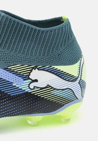 Puma football boot with a textured dark teal knit collar, vibrant lime accents, a pattern of blue and green stripes, and a white logo.