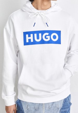 Haut à capuche blanc avec un grand graphique rectangulaire bleu portant le mot "HUGO" en texte blanc gras, capuche à cordon réglable et poche avant.