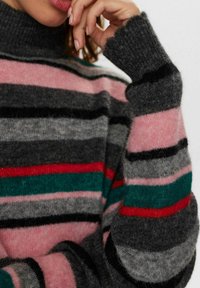 Prugasti pulover u sivoj, ružičastoj, crnoj i zelenoj boji. Visoki dizajn s turtleneck ovratnikom i rebrastim manžetama sa zaobljenim rubom. Mekana tekstura.