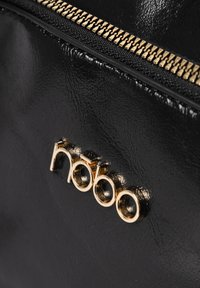 Borsa a tracolla nera in ecopelle con cerniera dorata e dettaglio logo lucido oro. La texture è liscia con una leggera lucentezza.