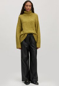 Olijfgroene, chunky gebreide turtleneck trui met een oversized pasvorm, gecombineerd met hoge taille, zwarte faux leren wijde broek.