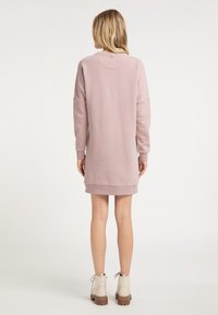 Vestido sudadera oversized rosa con mangas largas y escote redondo, presenta un dobladillo que se extiende ligeramente más allá de los muslos.