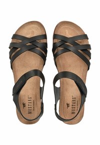 Schwarze Sandalen mit mehreren überkreuzten Riemen, einer gepolsterten braunen Innensohle und einem verstellbaren Riemen mit einem Markenakzent nahe der Ferse.