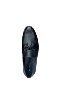 Mocasin de cuero negro con borlas, con un acabado suave, puntera redondeada y un forro interior suave. Nombre de la marca "WITTCHEN" visible en el interior.
