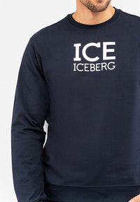 Felpa blu navy realizzata in tessuto morbido, con una grande grafica bianca "ICE ICEBERG" sulla parte anteriore e scollo a girocollo.