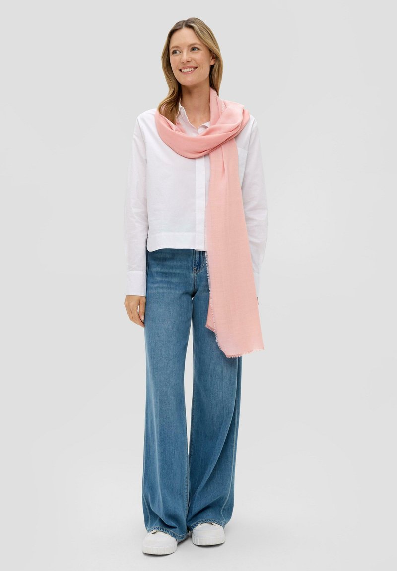Lichtroze sjaal rond de nek gedrapeerd, gecombineerd met een witte blouse met kraag en wijdvallende blauwe jeans. Gladde textuur en nietjes randen.