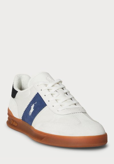 Tênis brancos em malha e camurça com detalhes azuis, apresentando uma sola de borracha e logotipo. Bico arredondado e design com atacadores.