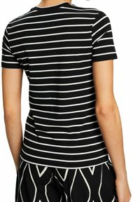Personne portant une chemise noire à manches courtes avec des rayures horizontales blanches et un pantalon noir avec des motifs géométriques blancs, vue de dos.