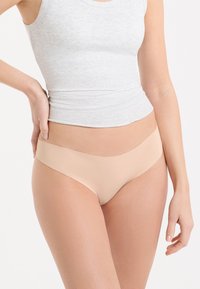 Sous-vêtements bikini seamless couleur nude avec une texture lisse et douce et une taille basse, assortis à un débardeur gris ajusté.