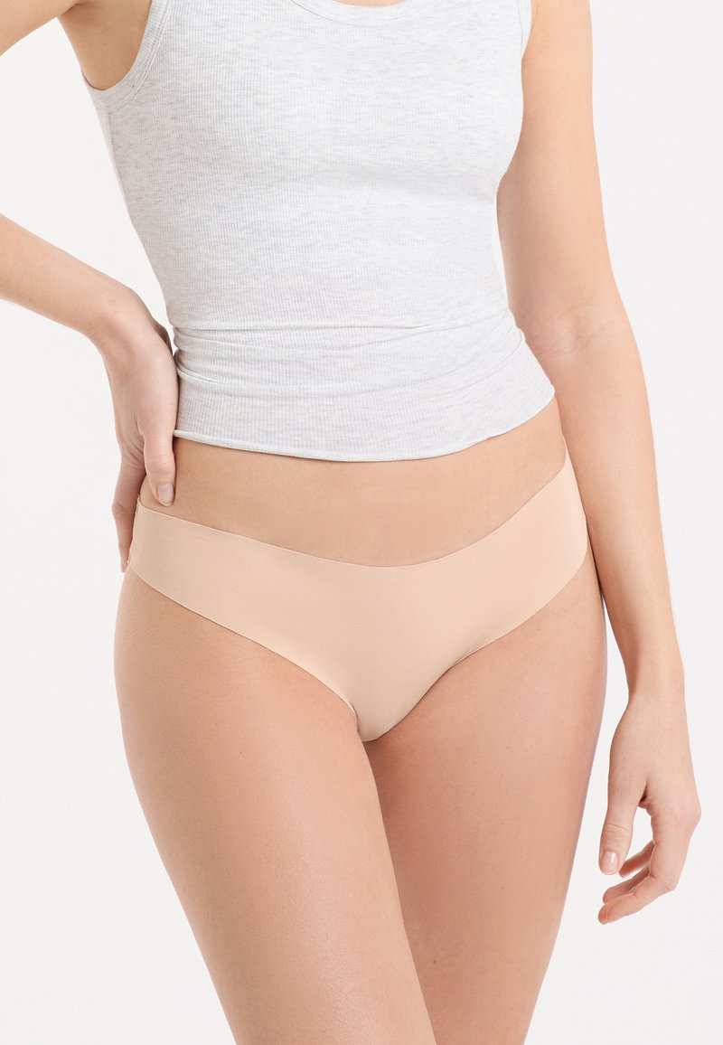 Sous-vêtements bikini seamless couleur nude avec une texture lisse et douce et une taille basse, assortis à un débardeur gris ajusté.