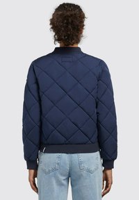 Chaqueta bomber acolchada de color navy con cuello redondeado, puños y dobladillo de canalé. Destaca por su patrón de diamantes y material ligero para brindar calidez.