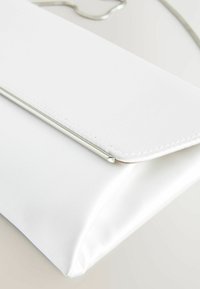 Fehér selyem clutch táska elegáns, háromszögletű formával, ezüst fém díszítéssel a fedélen és texturált felülettel.