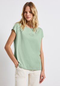 Mátově zelený krátký rukáv top s volným střihem a kulatým výstřihem. Obsahuje jemný potisk "PLAIN" na hrudi. Měkký bavlněný materiál.