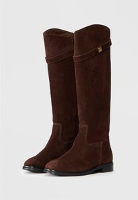 Stivali al ginocchio in suede marrone con suola nera piatta, caratterizzati da un risvolto e un piccolo accento metallico sul lato.